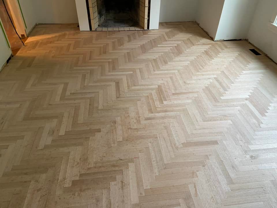 Empty herringbone wood floor in a room with a fireplace opening and white walls