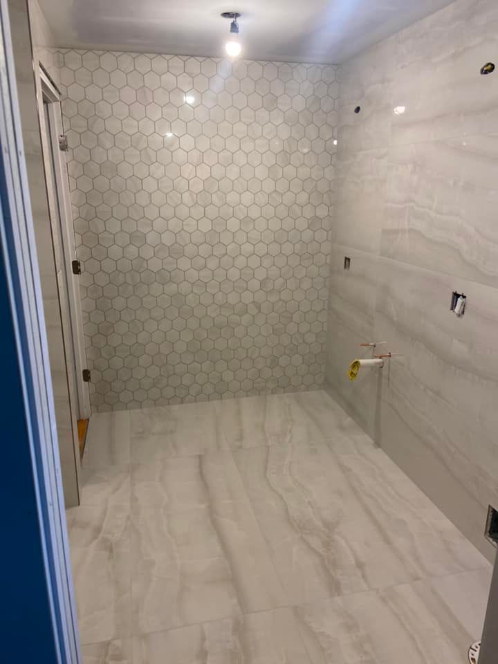 Empty bathroom under construction with white tile walls, marble-look floor, and a single ceiling light.