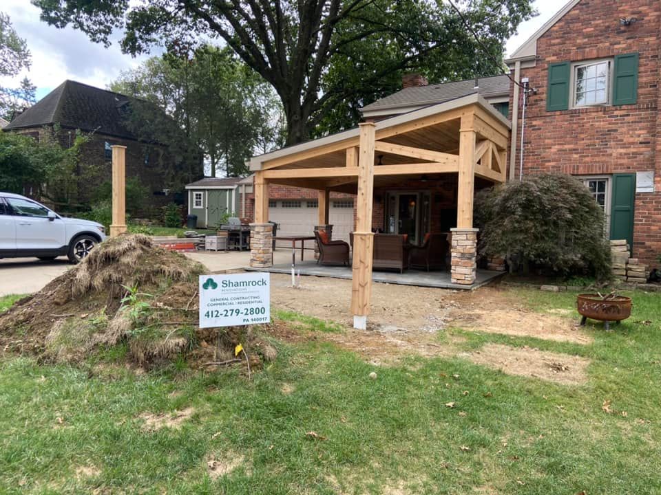 Porch under construction beside a brick house, with a sign in the front yard.