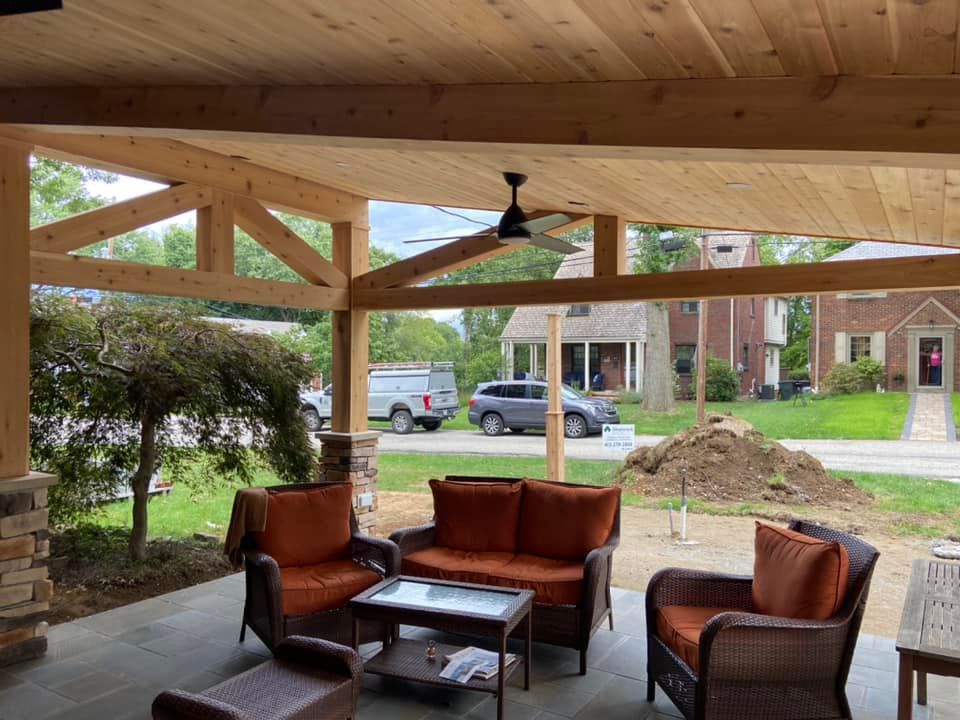 Covered porch with wicker chairs and sofa, coffee table, and ceiling fan overlooking a street and parked vehicles