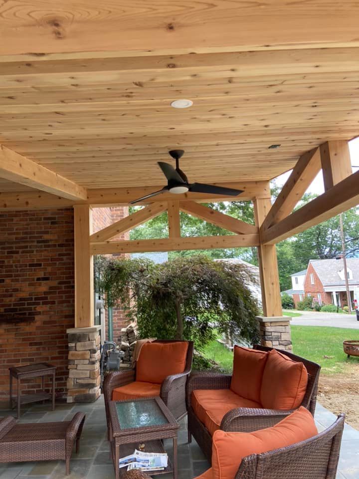 Covered porch with orange outdoor seating, ceiling fan, and brick and wood accents overlooking a yard.