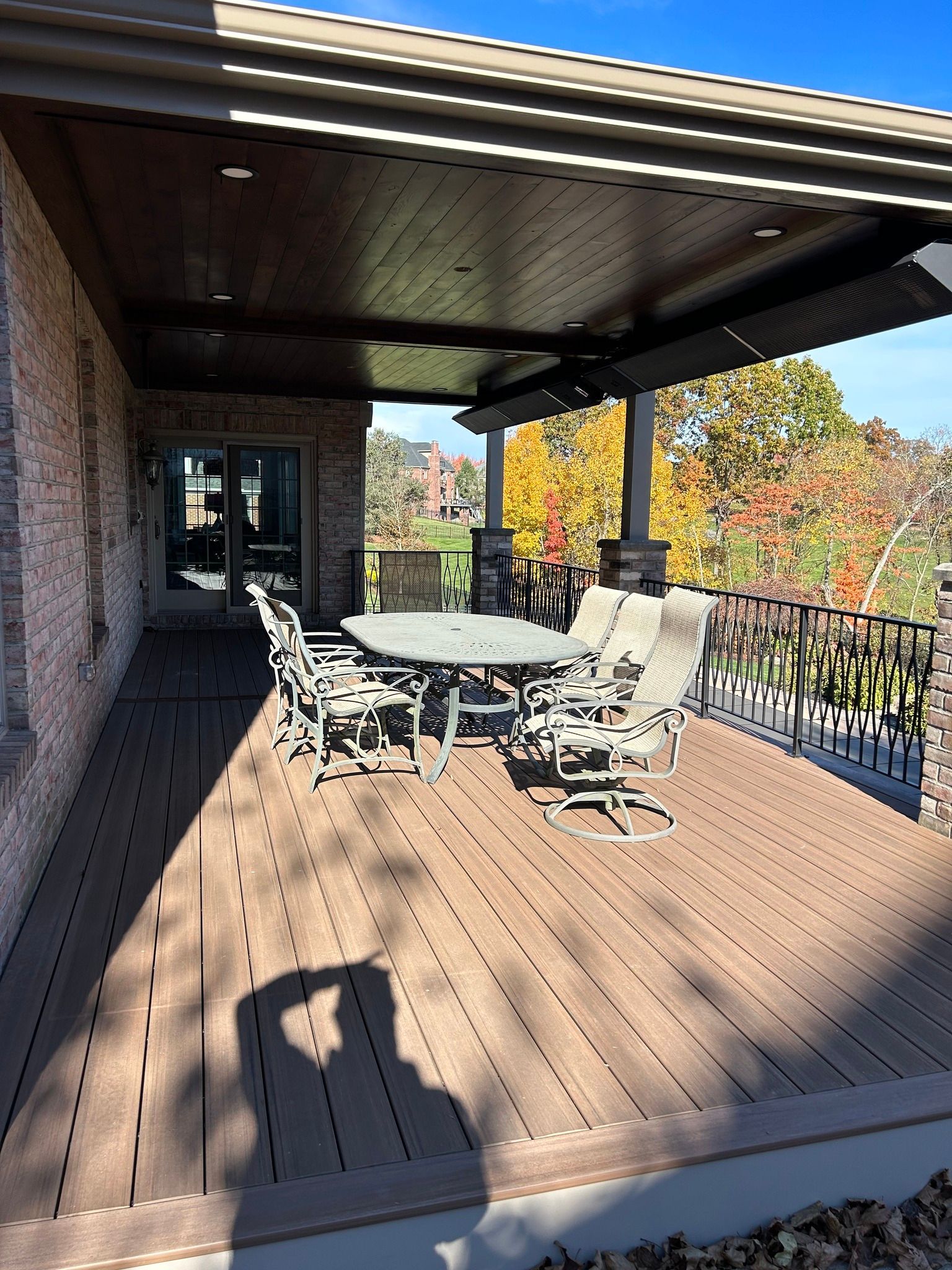 Covered wooden deck with outdoor dining table, chairs, and railing overlooking autumn trees