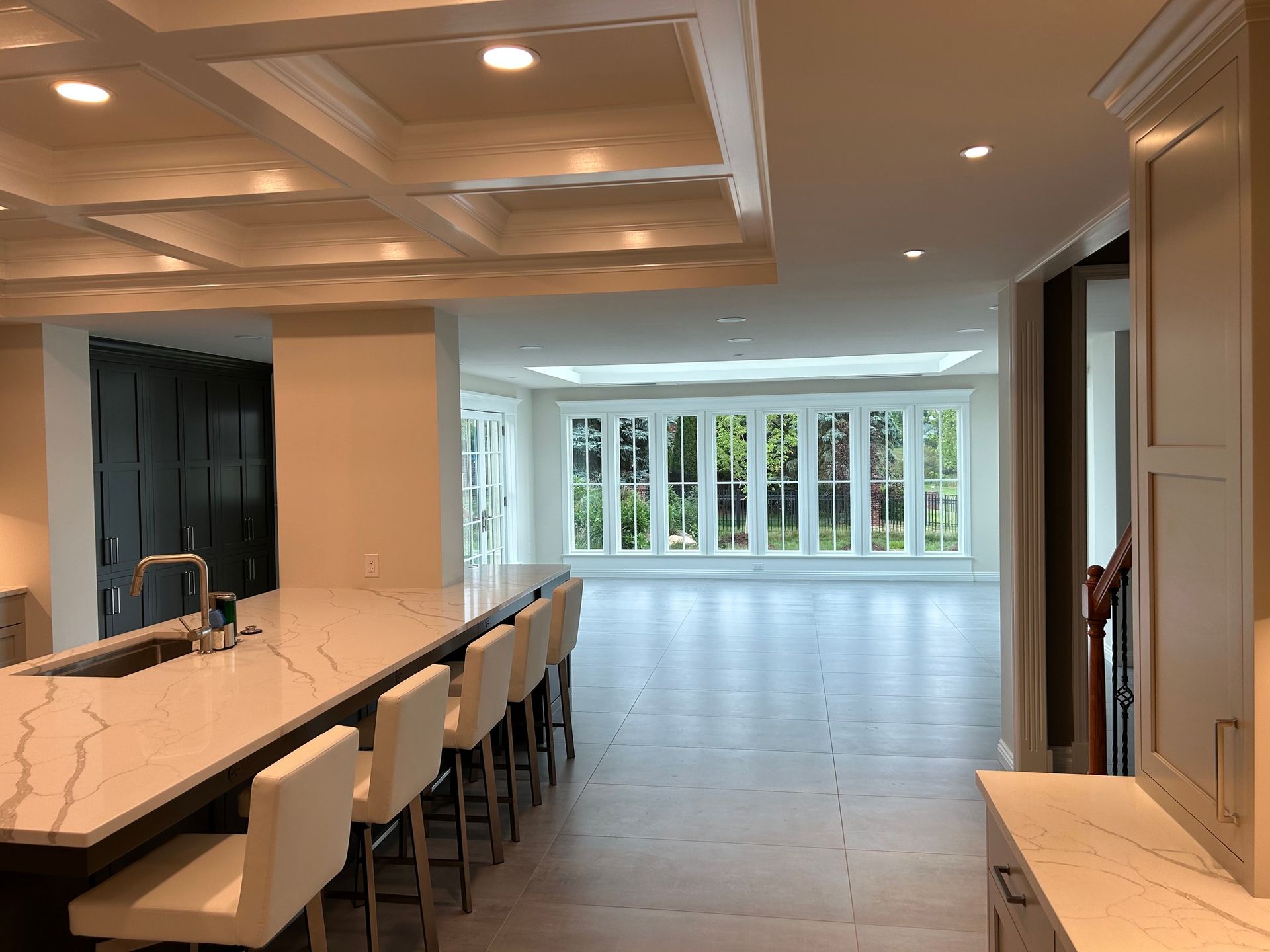 Modern kitchen with a long island, bar stools, recessed lighting, and a bright open room with large windows