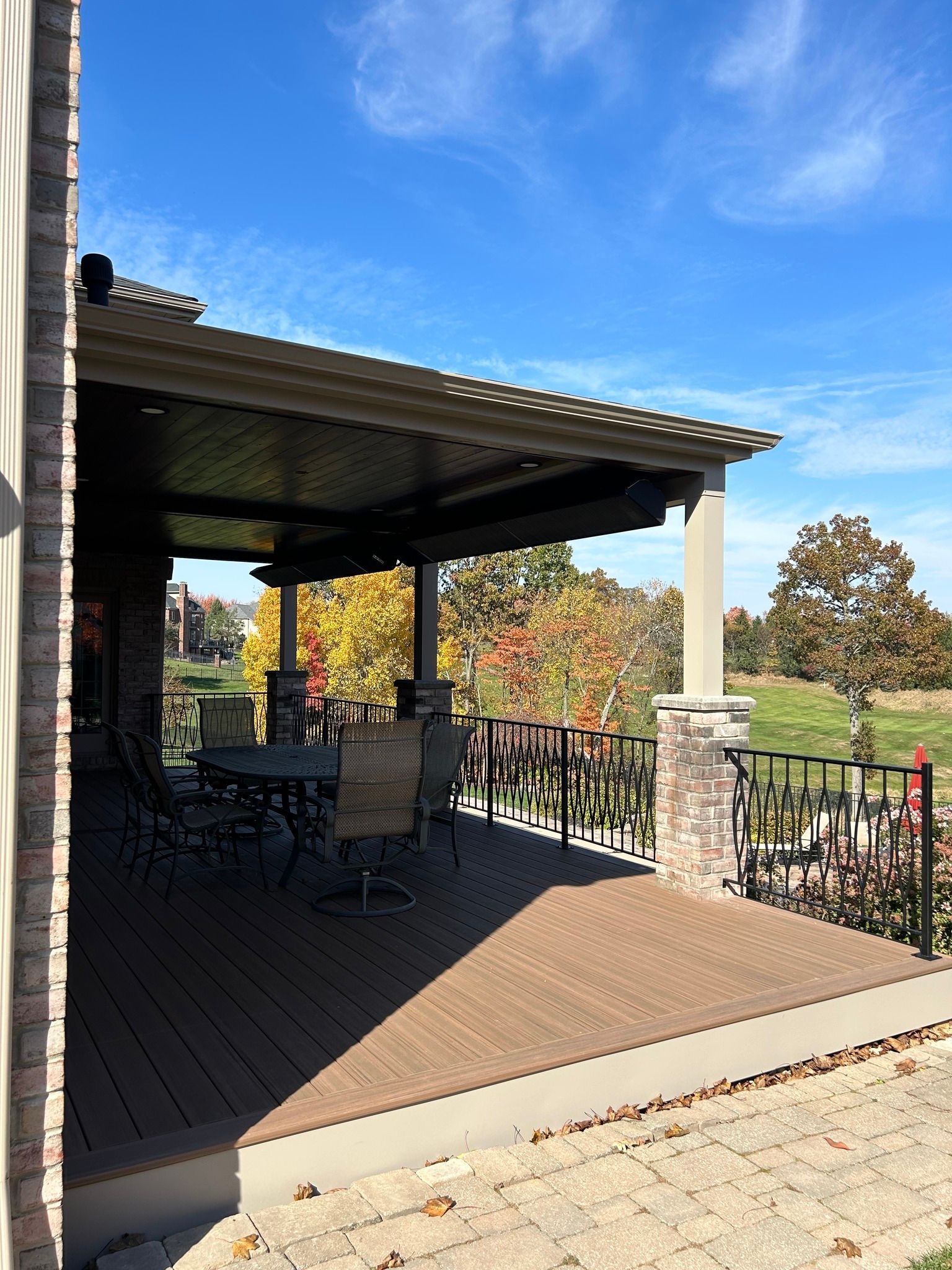 Covered patio deck with black chairs, railing, and view of trees under a blue sky