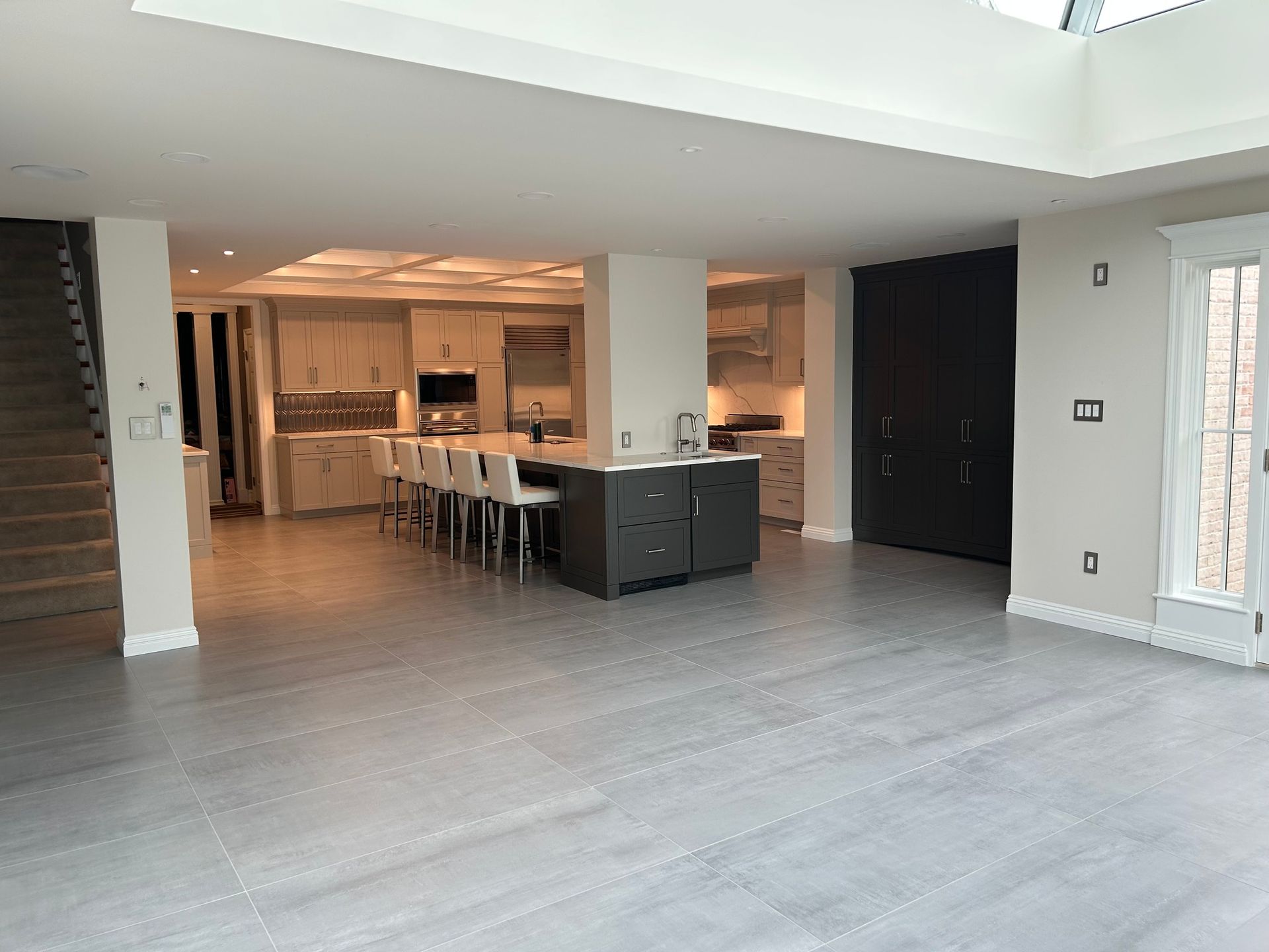 Open-plan modern living room with kitchen island, gray floors, and large windows