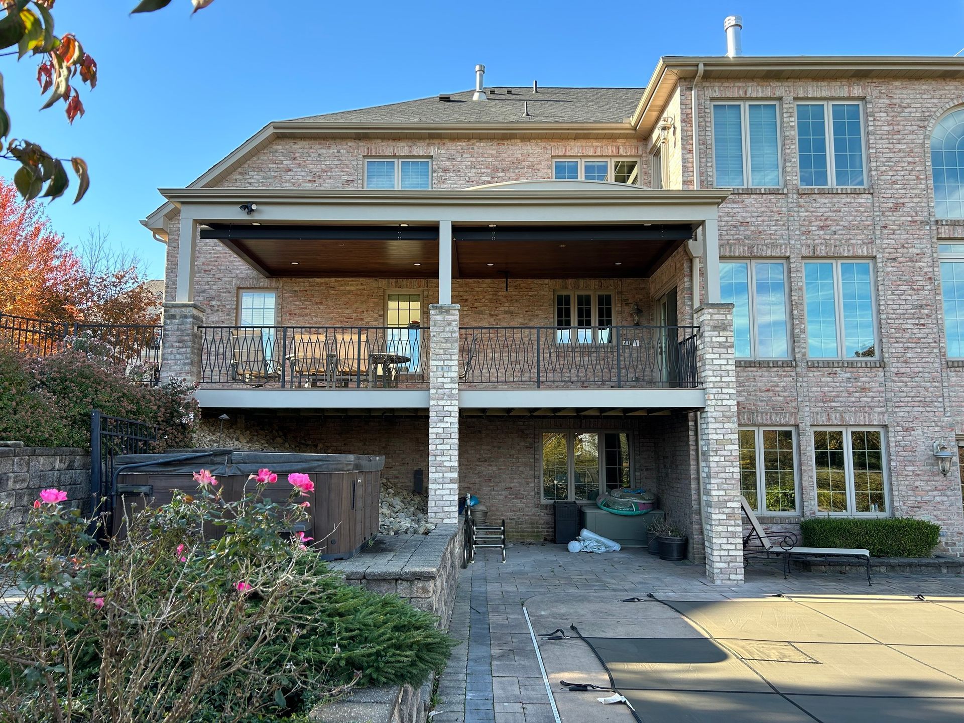 Brick house with covered balcony, stone pillars, and a backyard patio under a blue sky