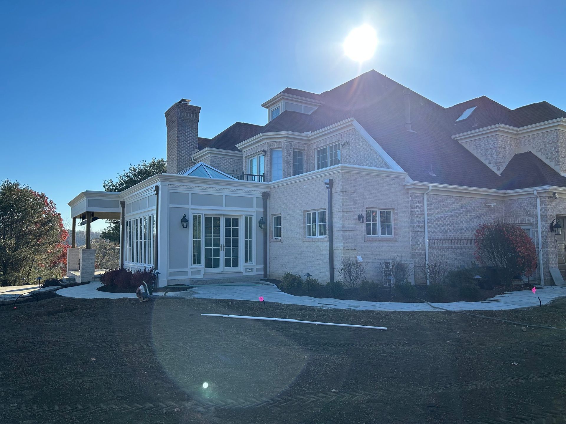Large stone house with a porch and dormer windows in bright sunlight, with a driveway in front