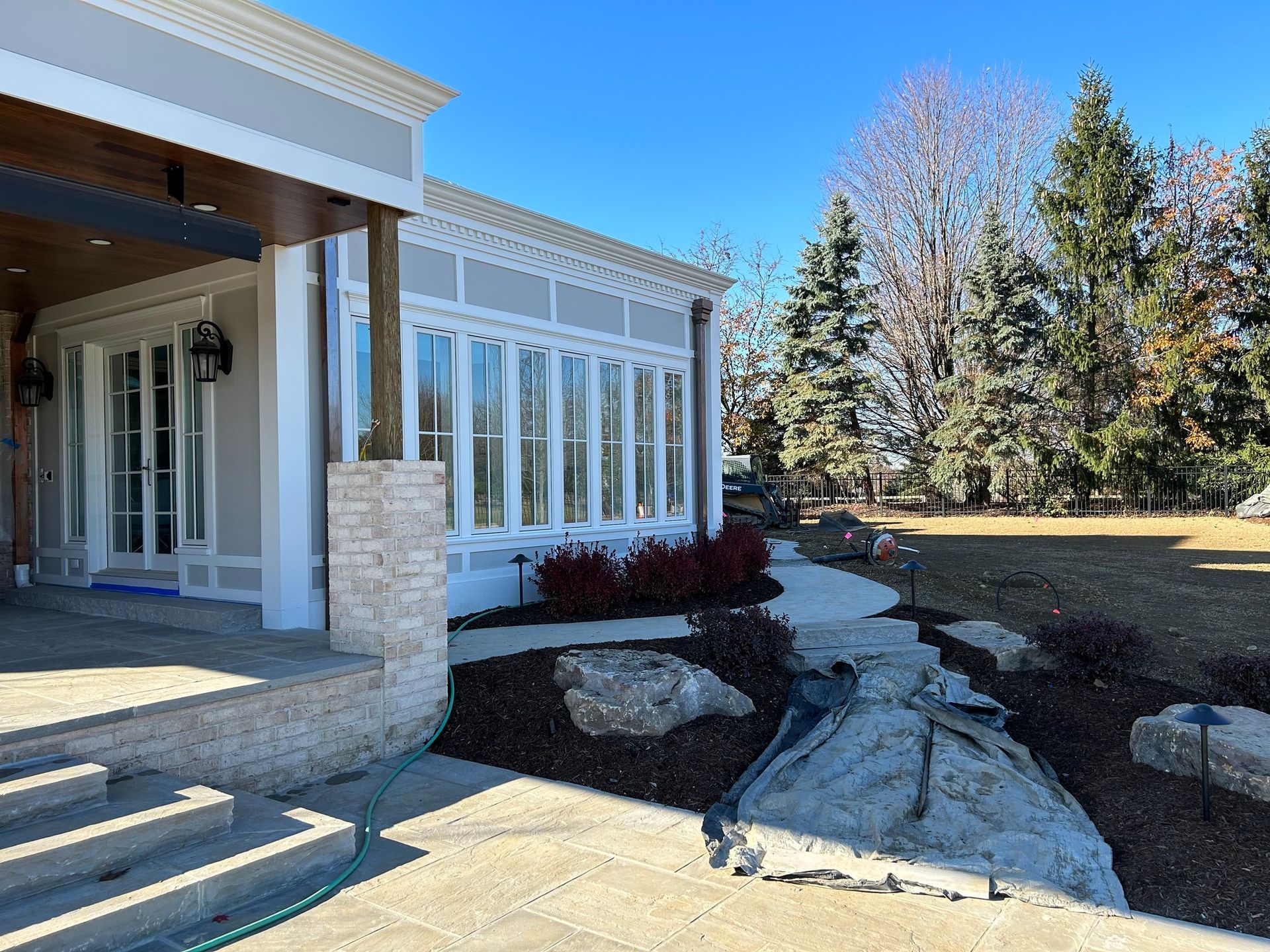 Front entrance of a house with white trim, steps, and landscaped rocks in a sunny yard