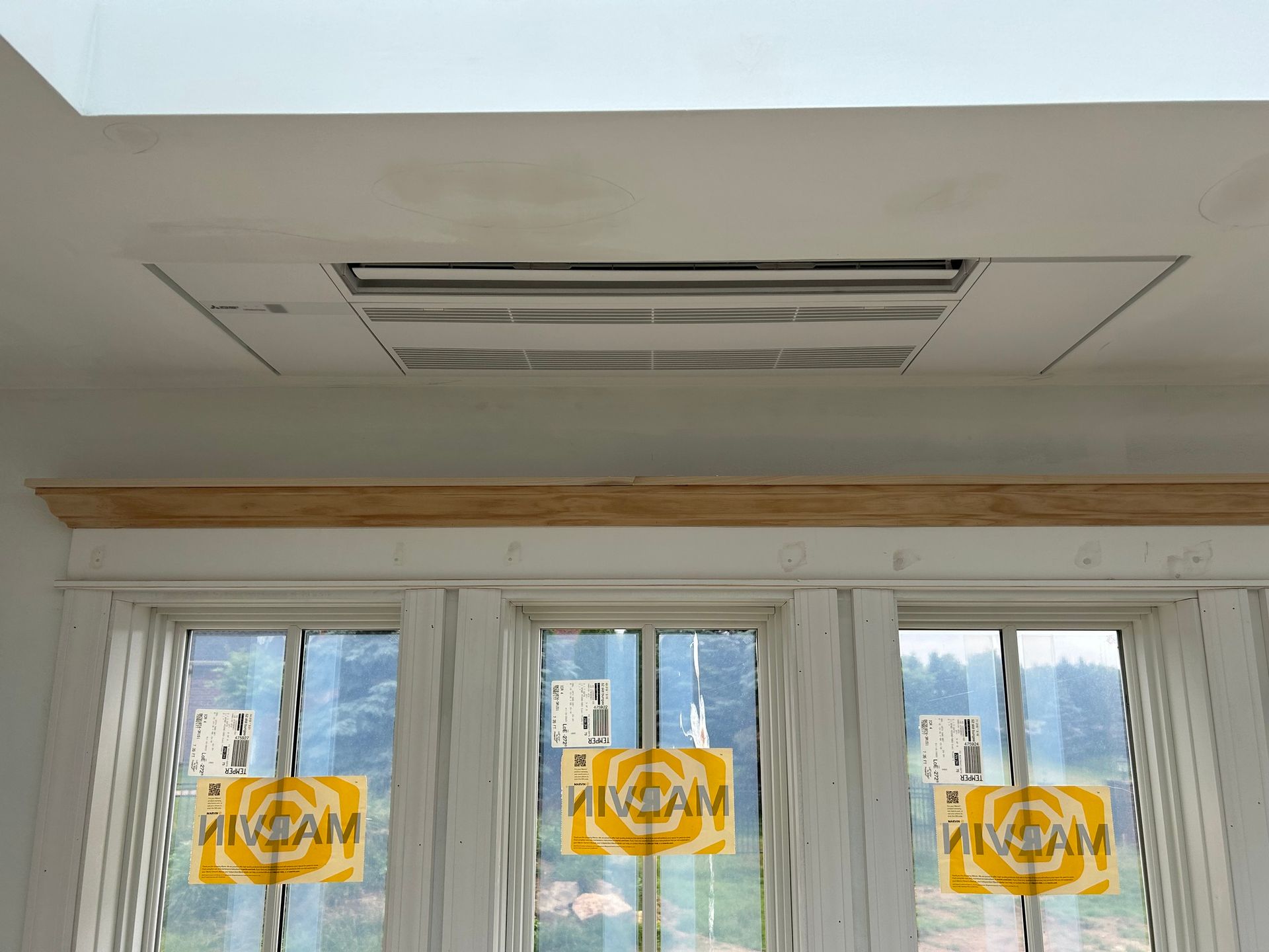 White ceiling with a rectangular vent above three windows with yellow signs