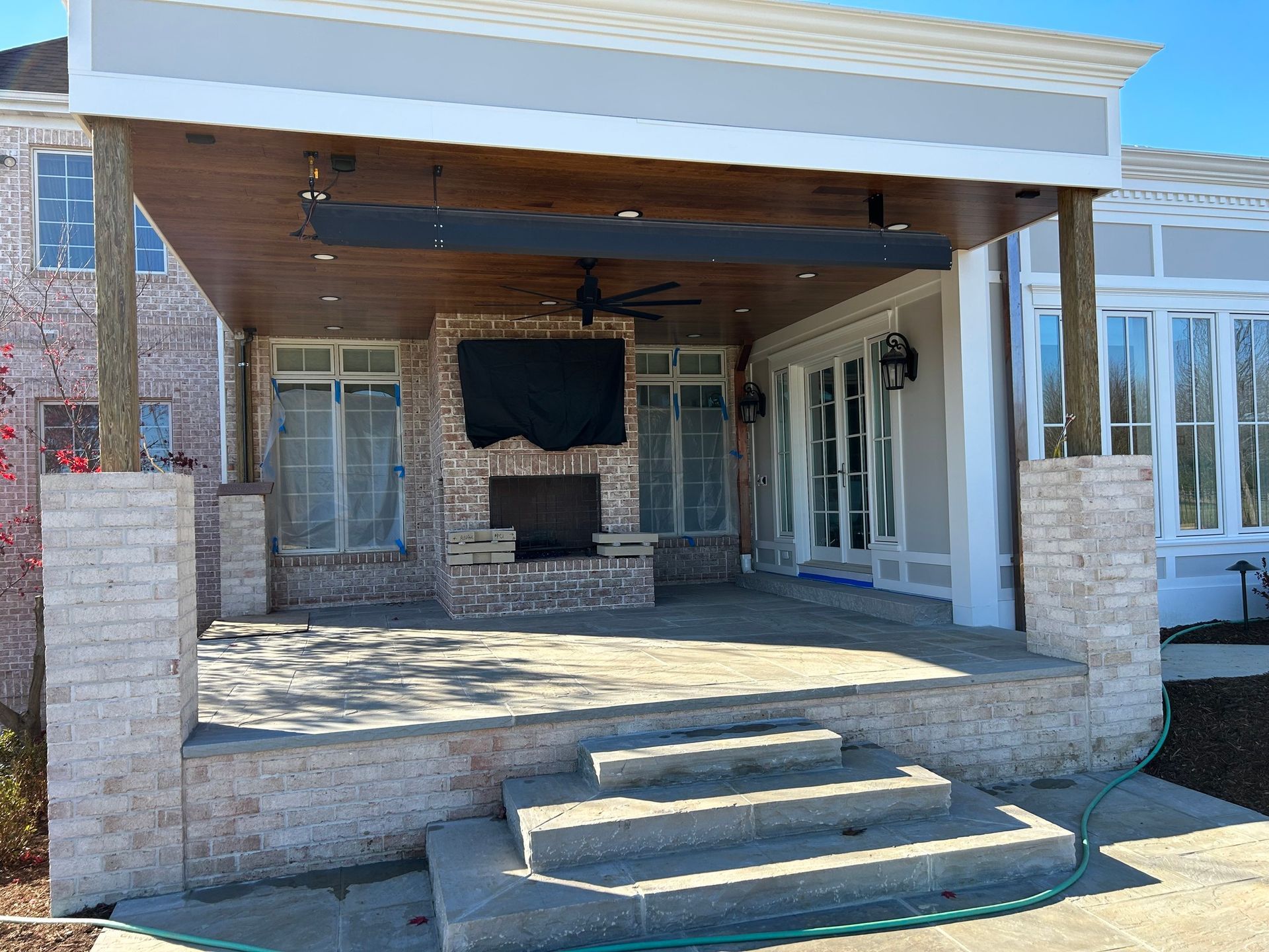 Front porch with stone columns, steps, and a mounted TV on a brick wall under a covered patio.