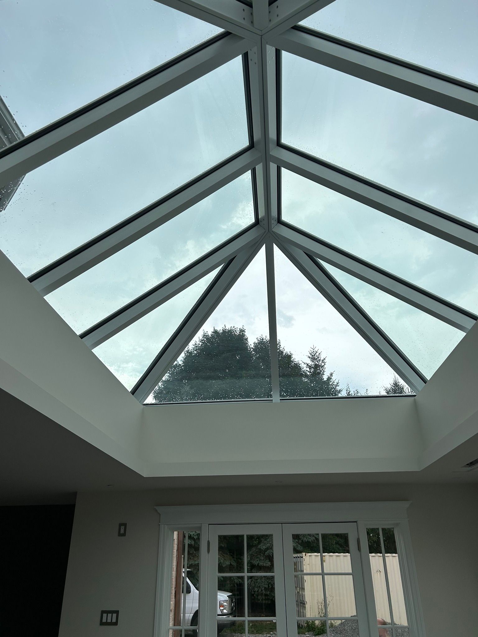 Glass ceiling with metal beams over a bright room, seen from below.