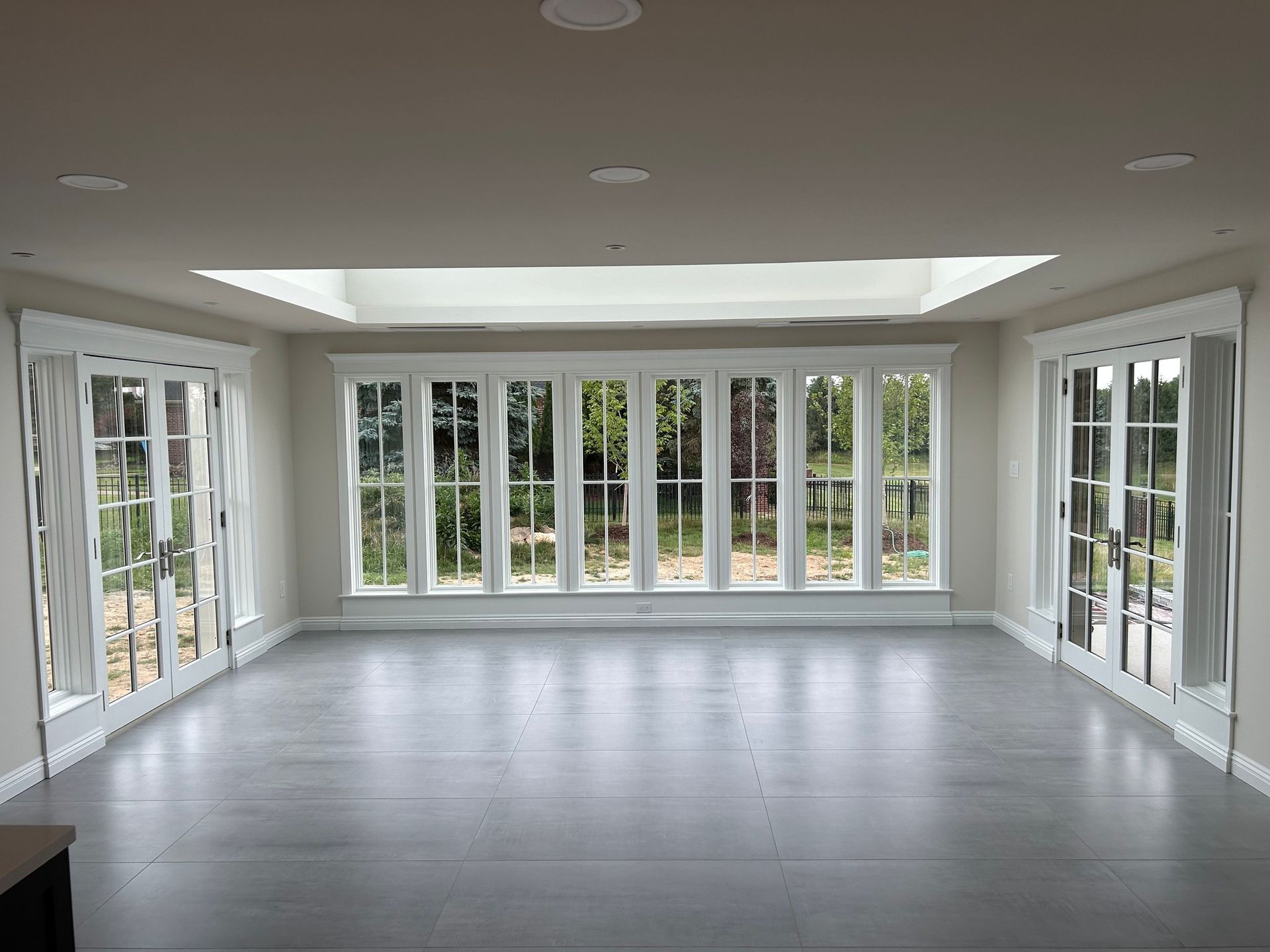 Bright empty sunroom with white walls, gray floor, and large windows on three sides.