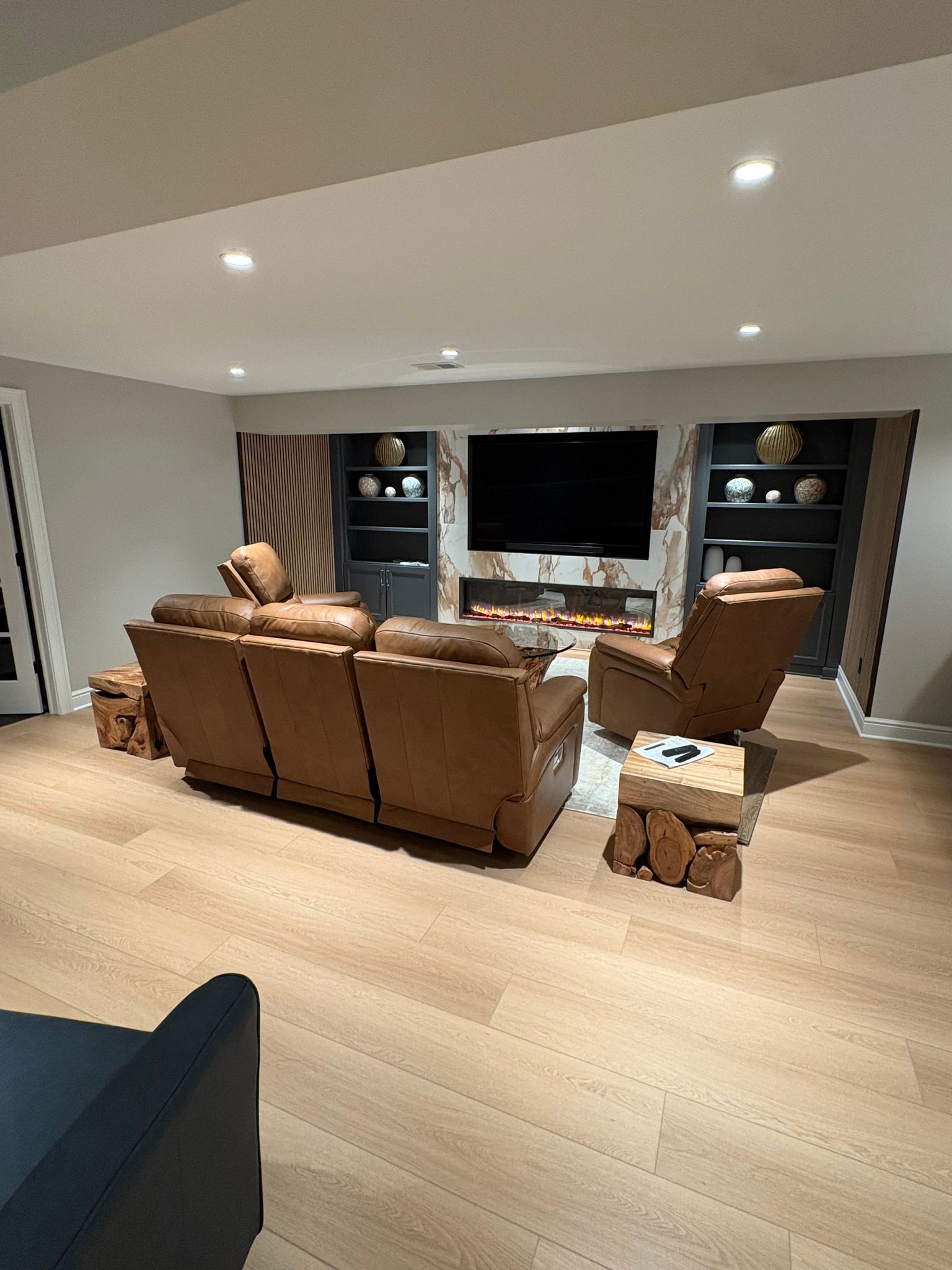 Modern living room with tan leather sofas, recliners, built-in shelves, and a wall-mounted TV.