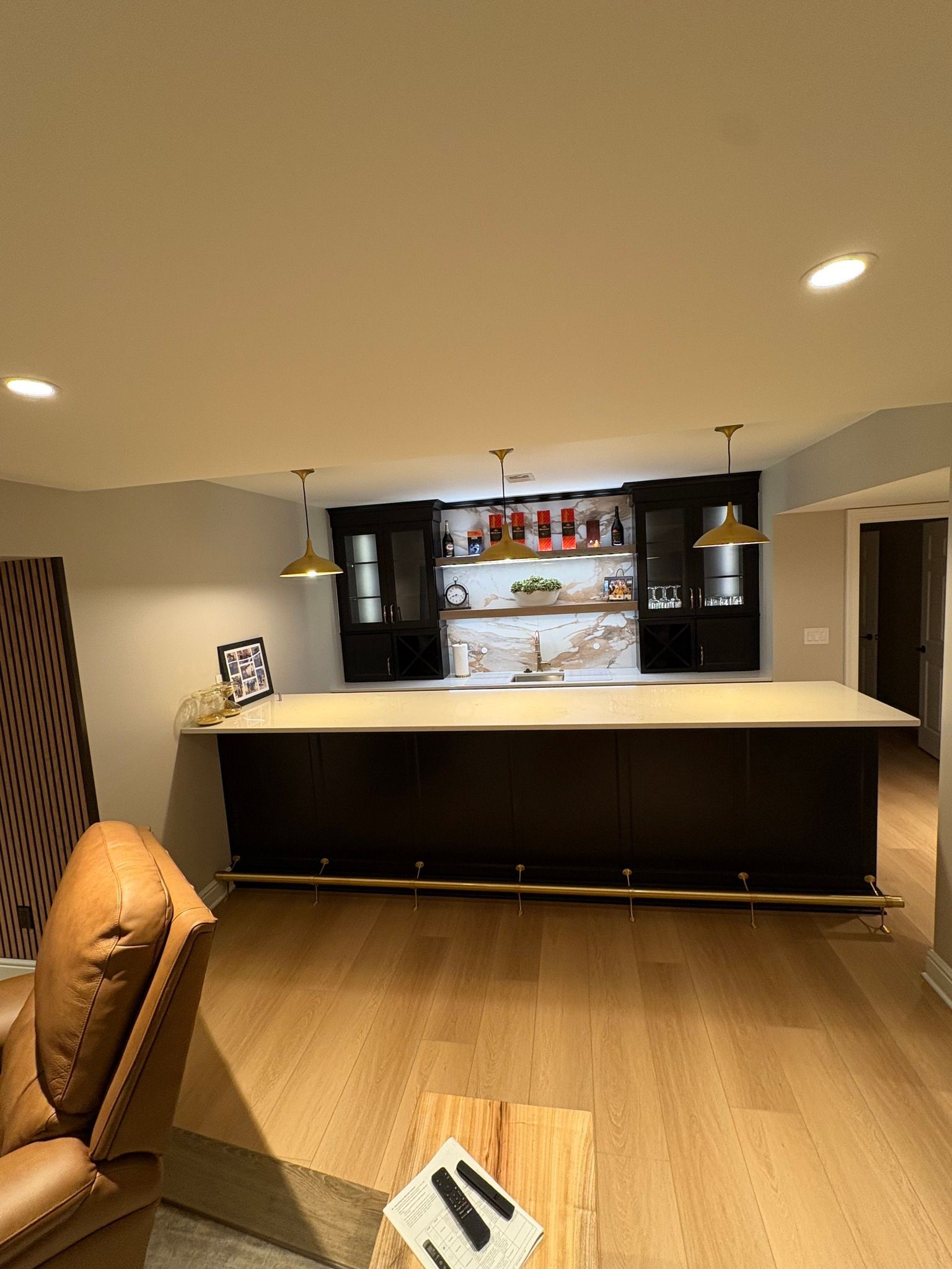Modern kitchen with black island, wood floor, pendant lights, and open shelving against a gray wall