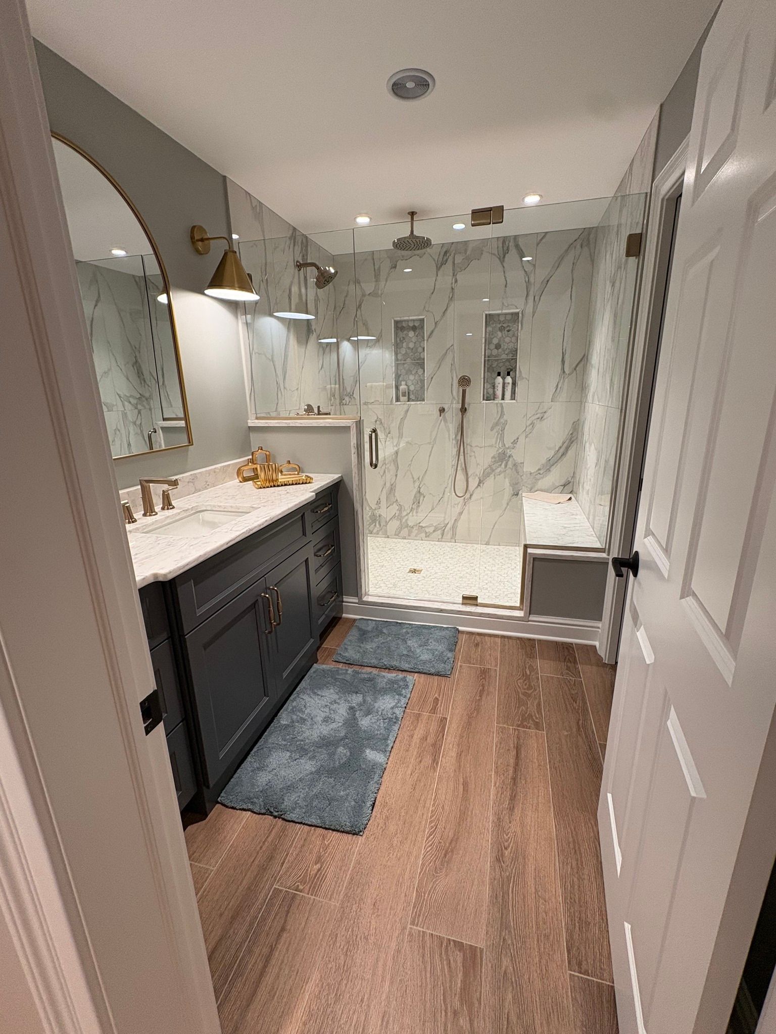 Narrow bathroom with dark vanity, white shower, wood floor, and blue bath mats.