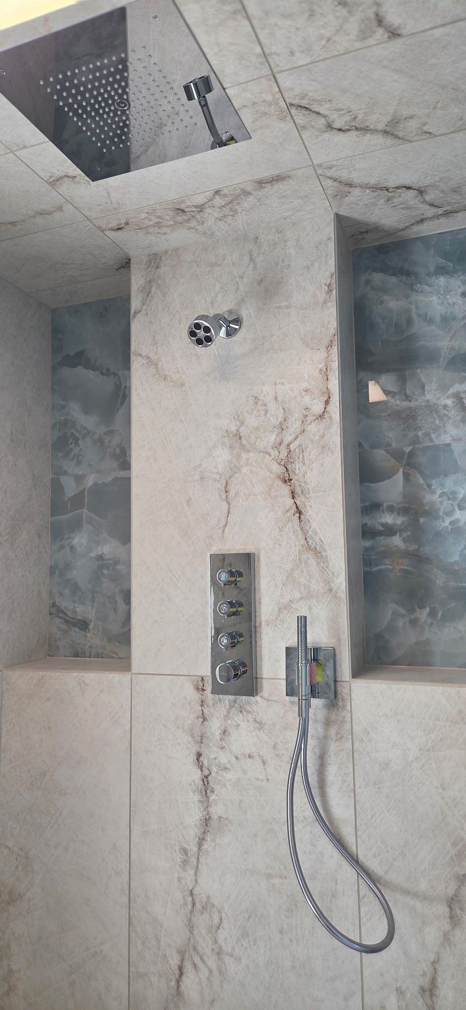Unfinished bathroom with tiled shower wall, recessed niche, and exposed plumbing fixtures.