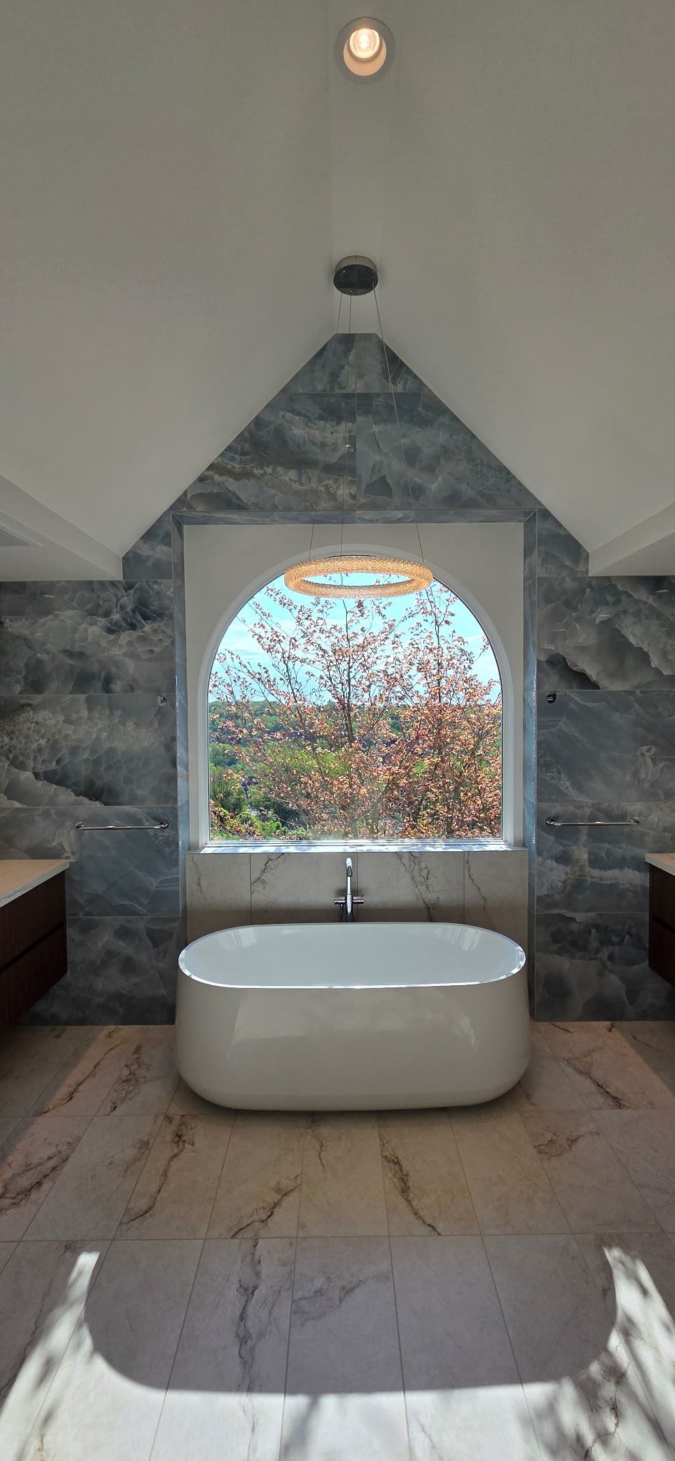 Modern bathroom with a freestanding tub in front of a stone-framed arched window and patterned tile wall