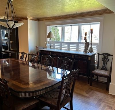Formal dining room with a polished wooden table, carved chairs, and a sideboard under a bright window