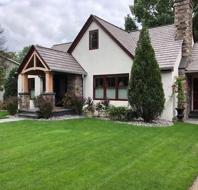 Suburban house with stone chimney, white siding, red-trimmed windows, and a green lawn