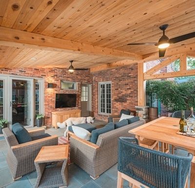Covered brick patio with wicker seating, wood ceiling, fireplace, and dining table outdoors