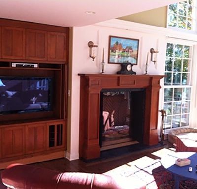 Living room with wooden fireplace mantel, built-in TV cabinet, and large windows