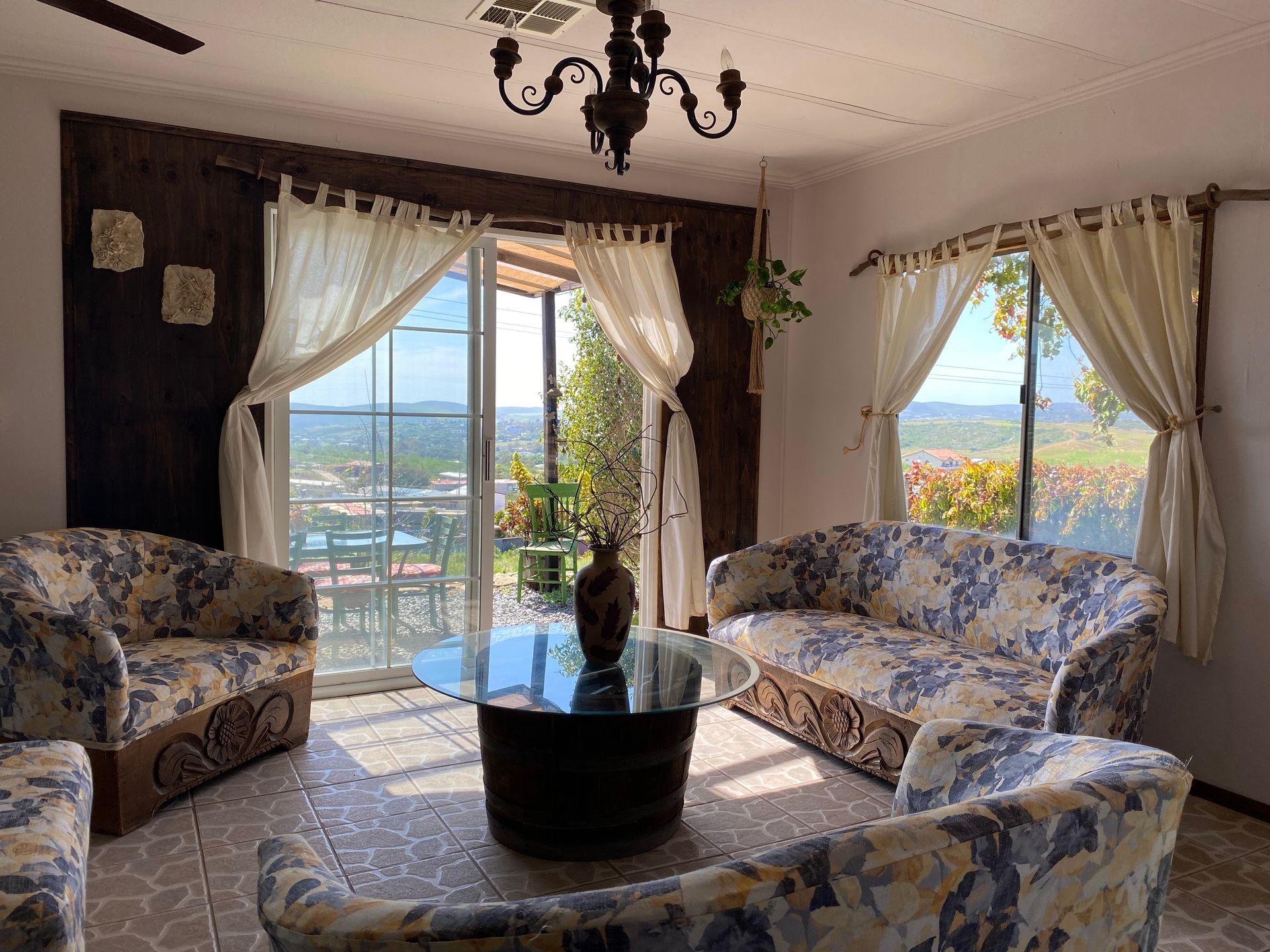Sala de estar con sofás estampados con motivos florales, mesa de centro de cristal, lámpara de araña y vista al océano a través de las cortinas abiertas.