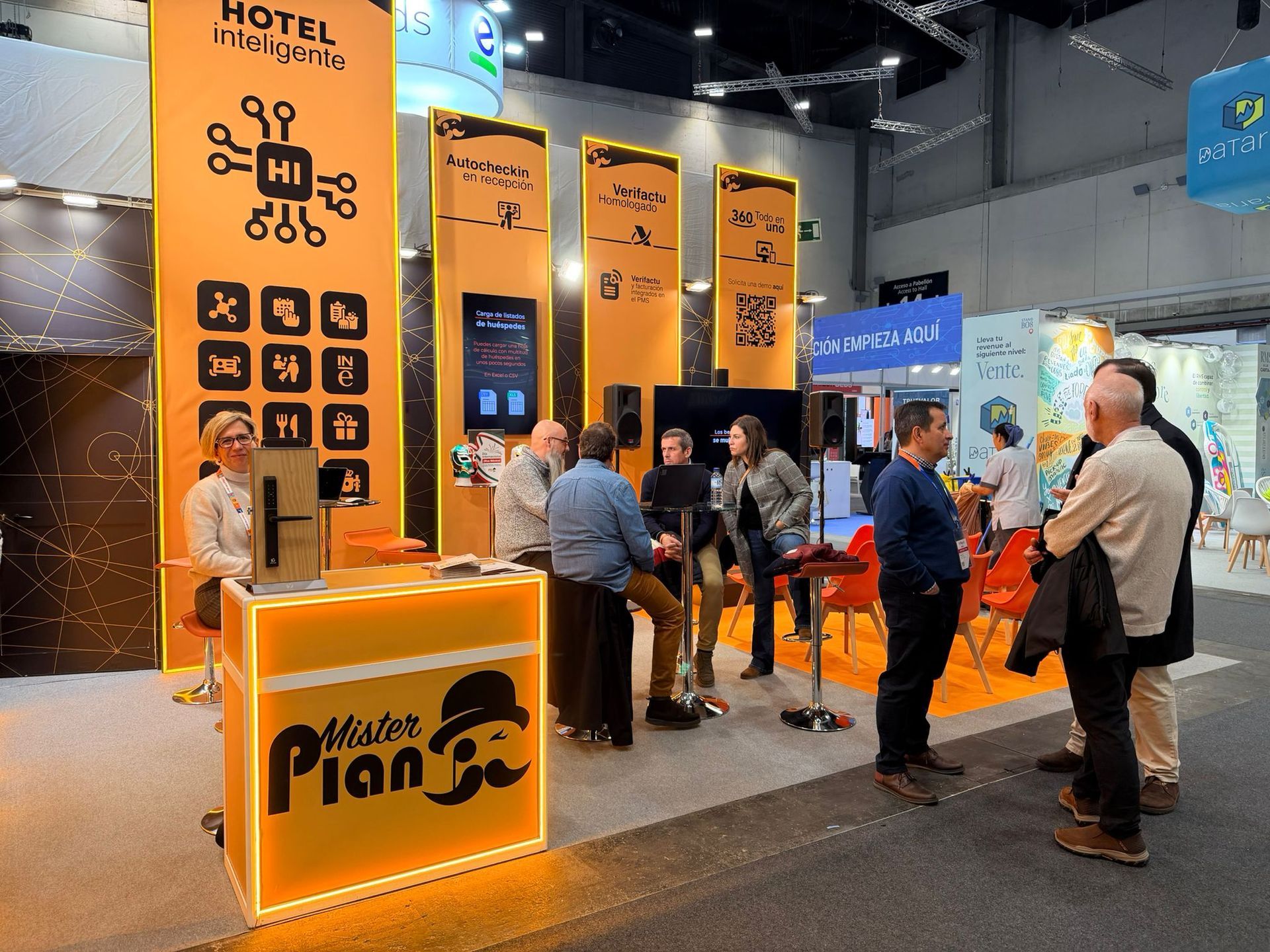 Stand de exposición del hotel Orange con gente charlando y de pie alrededor de los mostradores de exhibición.