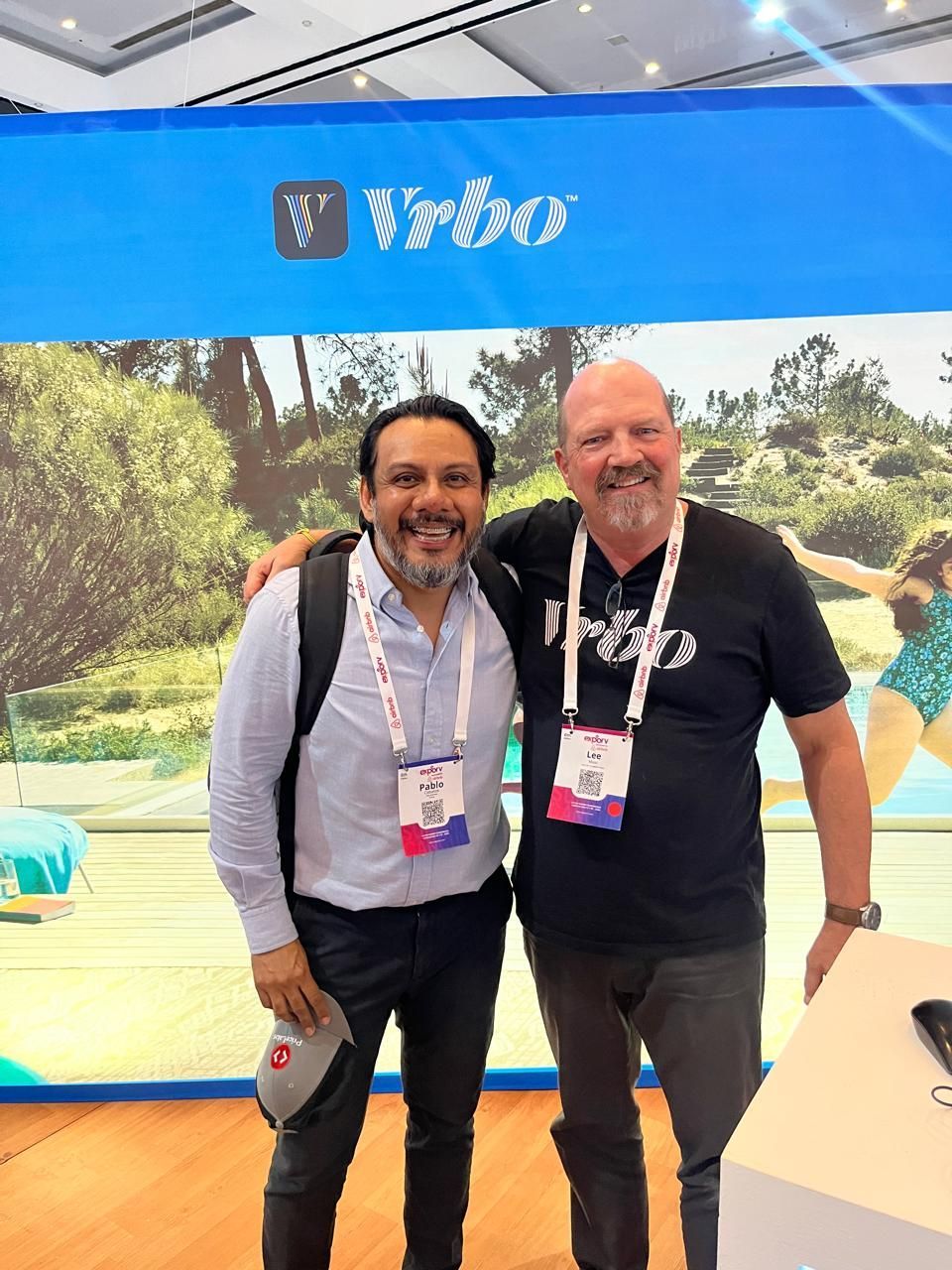 Dos hombres sonriendo y posando en un stand de WEX con un telón de fondo azul.