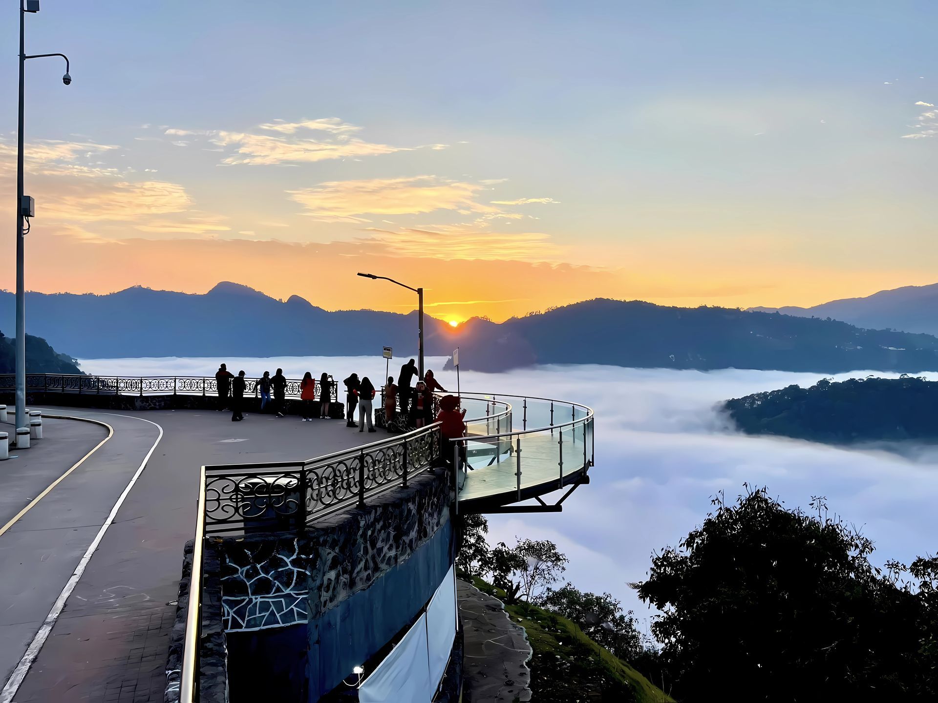 Amanecer sobre las montañas con gente en una carretera sobre un valle de nubes.