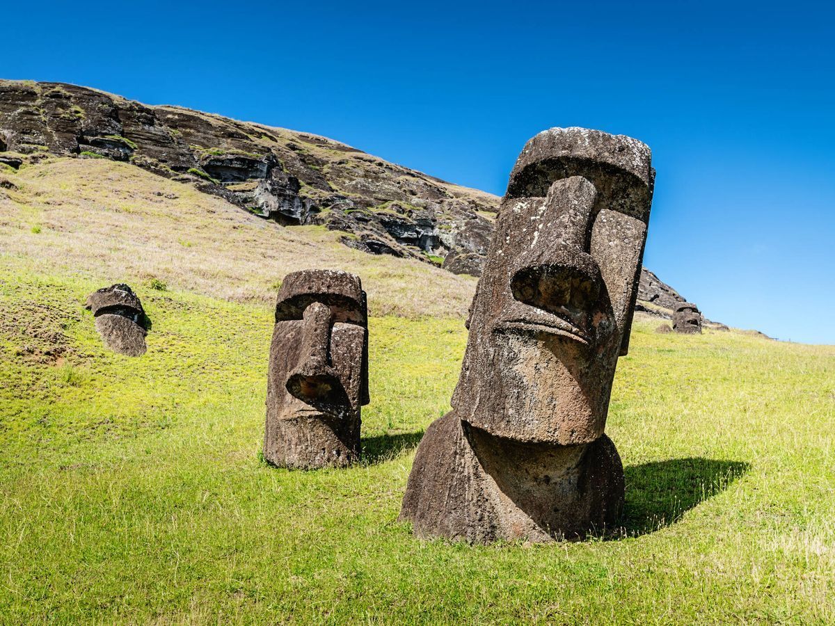 Tres estatuas Moai en una ladera cubierta de hierba bajo un cielo azul despejado.