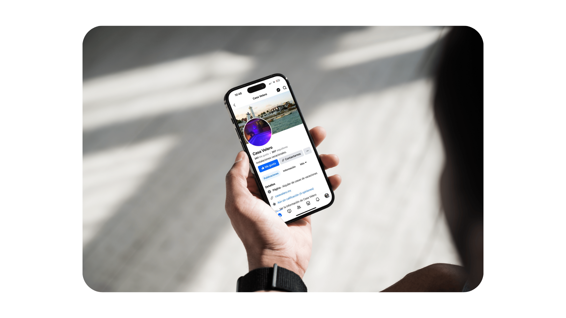 Una mano sostiene un teléfono inteligente que muestra un feed de redes sociales en una habitación luminosa.