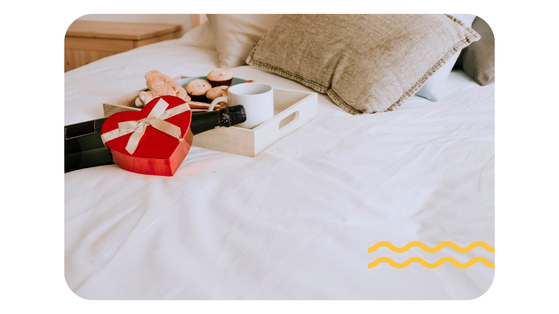 Cajas de regalo y una pequeña muñeca en una cama blanca con almohadas beige y un gráfico ondulado amarillo.