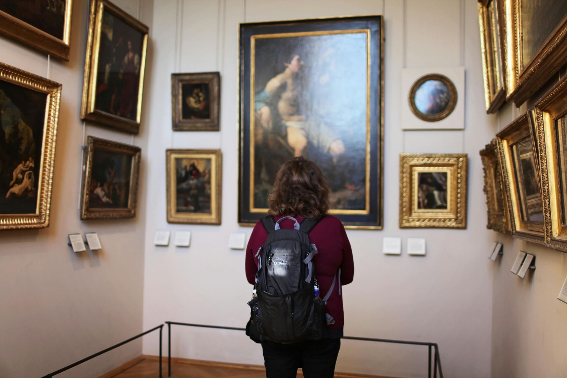 Una persona con mochila observa cuadros enmarcados en una sala de una galería de arte.