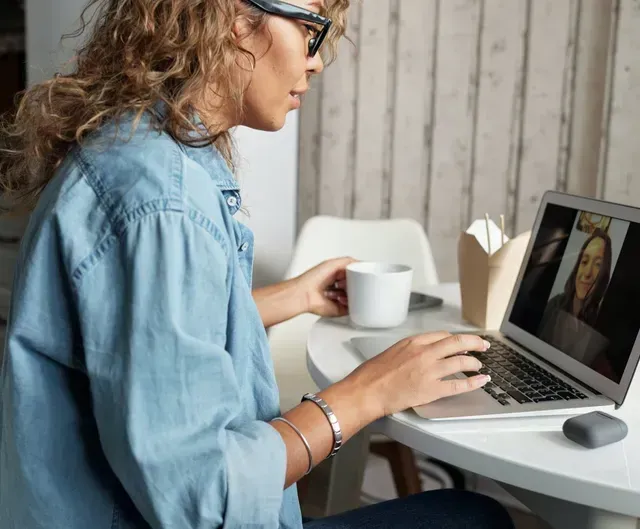 Mujer con gafas usando un portátil en una mesa blanca con una taza y una caja de pañuelos.