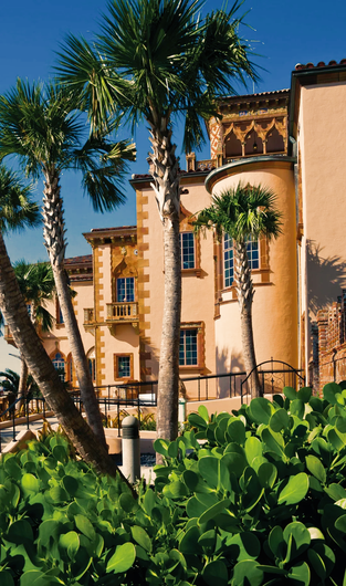 Palm trees frame a peach-colored building with ornate details and blue sky.