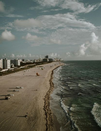 Beach with buildings in the distance, waves crashing, cloudy sky.