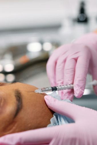 Person receiving a facial injection with a syringe by a person wearing pink gloves.
