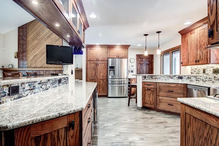A kitchen with wooden cabinets , granite counter tops , stainless steel appliances and a flat screen tv.