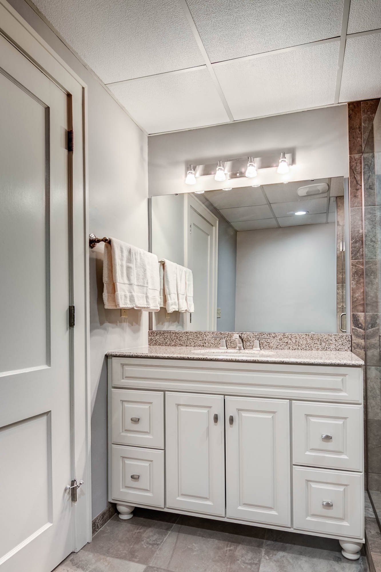A bathroom with a sink , mirror and towels hanging on the wall.