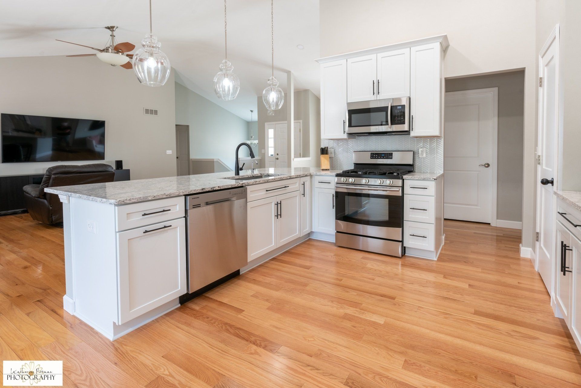 A kitchen with white cabinets , stainless steel appliances , hardwood floors and a large island.