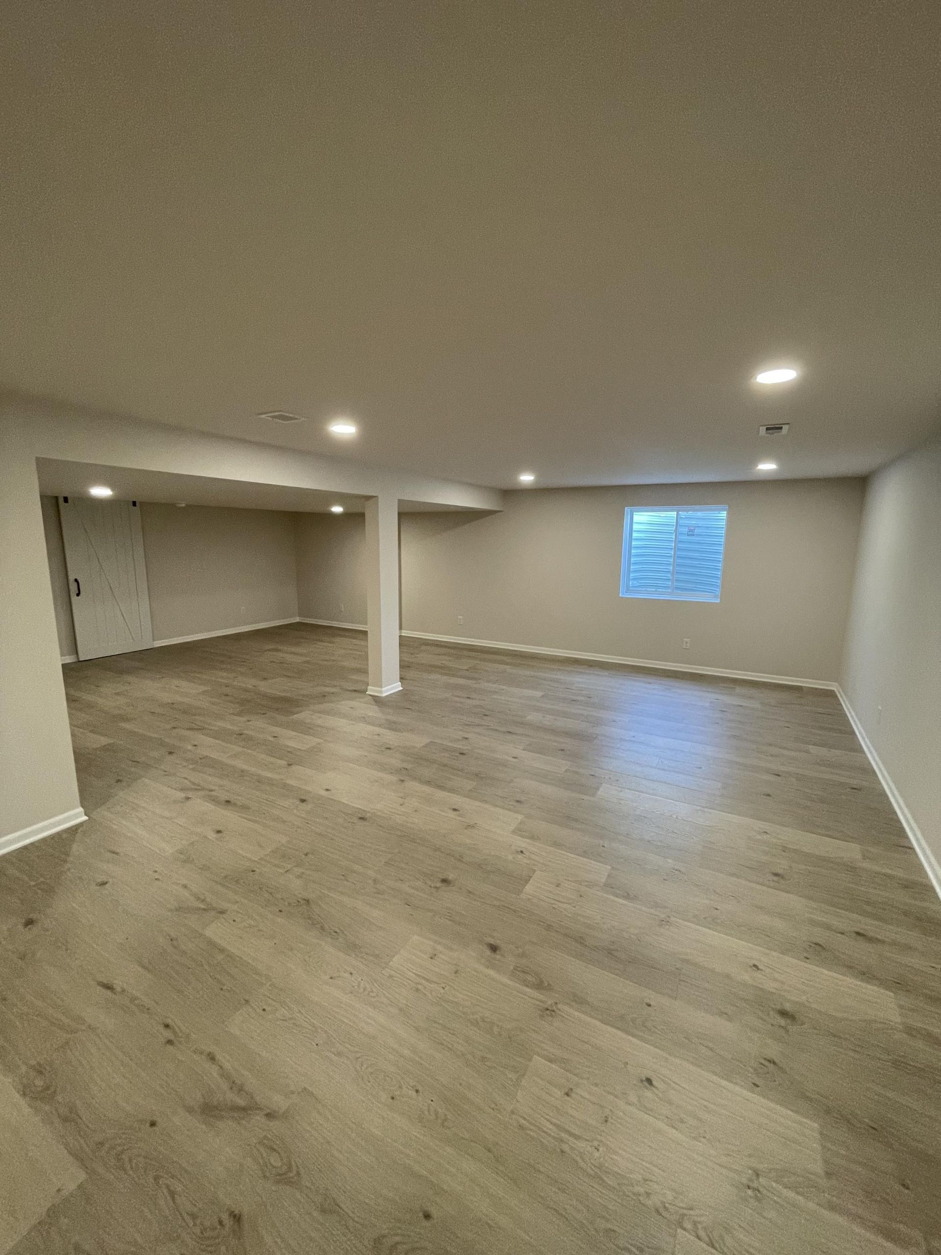 An empty basement with hardwood floors and a window.