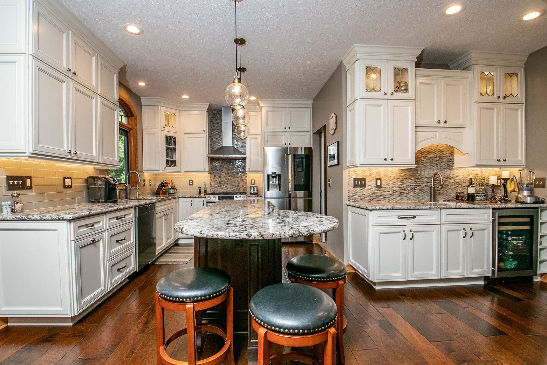 A kitchen with white cabinets , granite counter tops , stools and a large island.