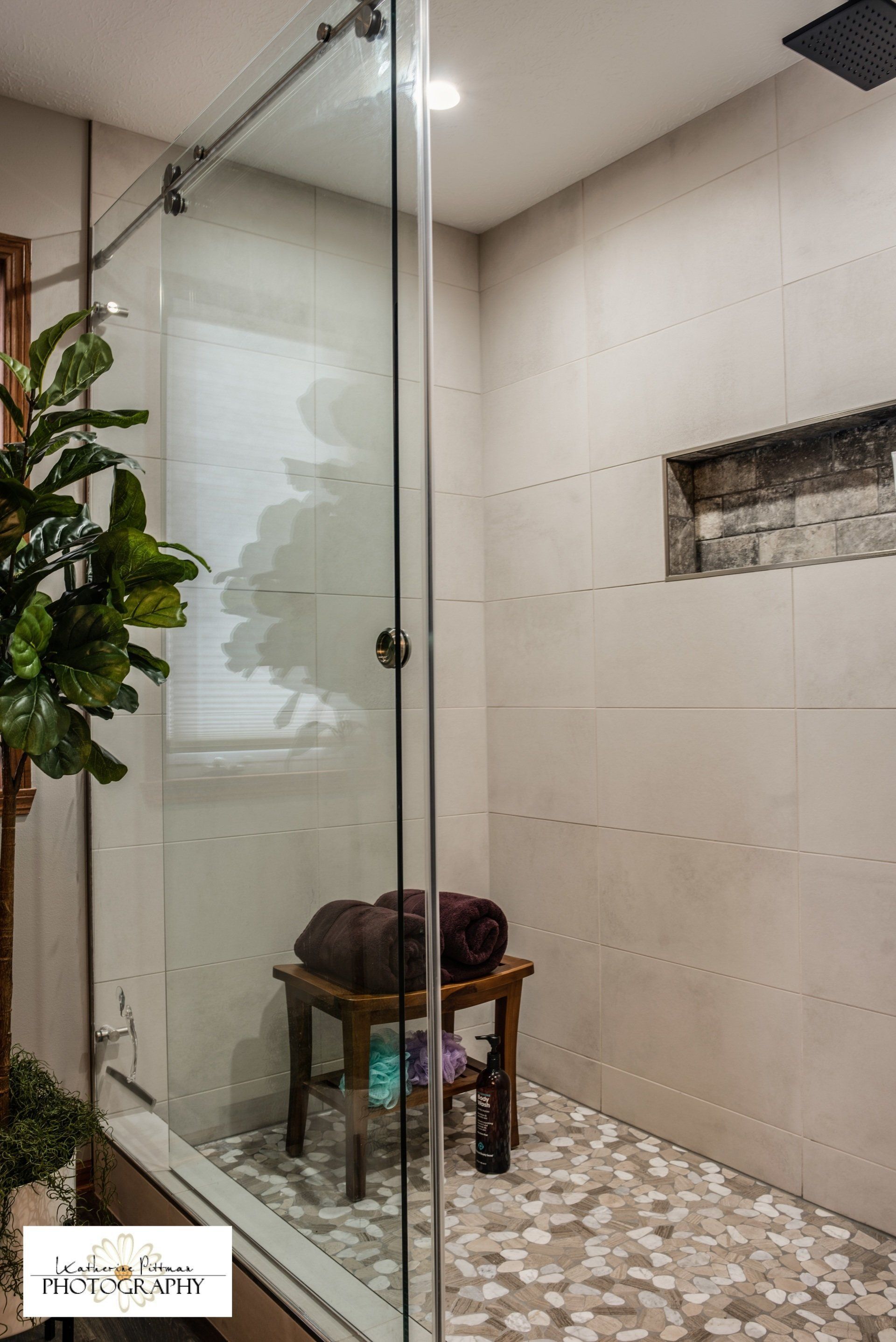 A bathroom with a walk in shower and a bench with towels on it.