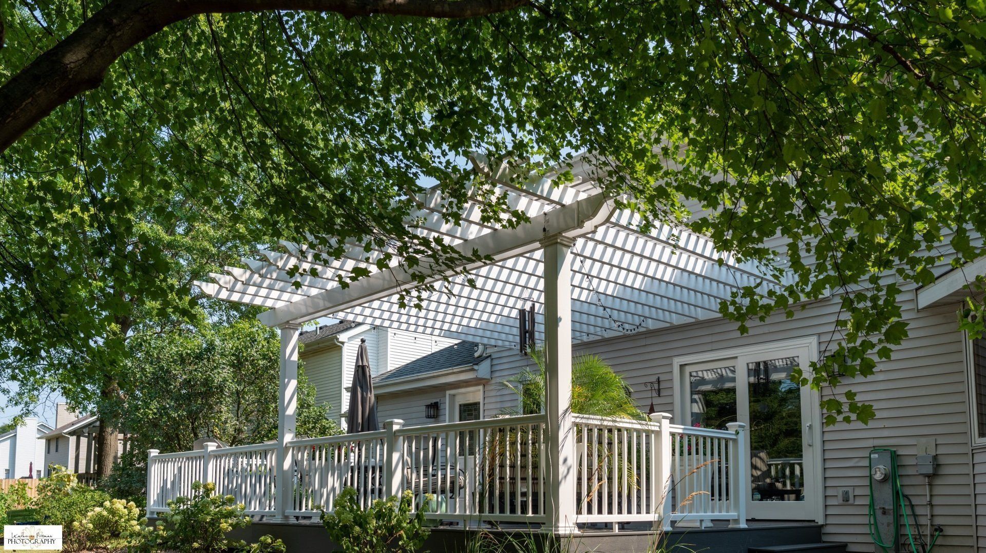 A white house with a white pergola over a deck.