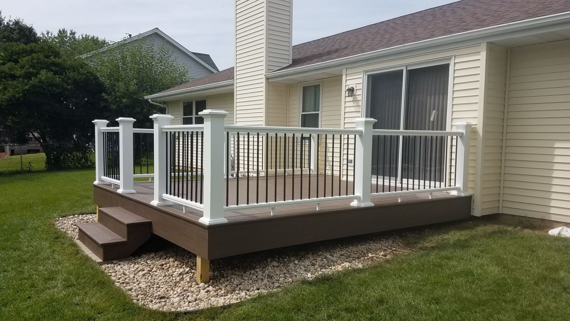 A deck with a white railing is in the backyard of a house.
