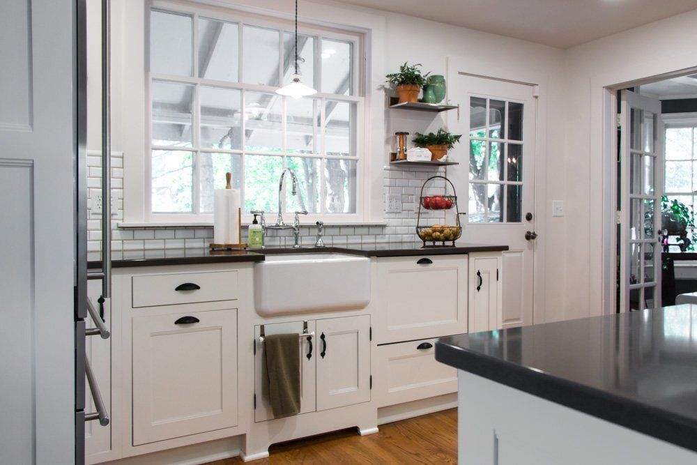A kitchen with white cabinets , black counter tops , a sink and a window.