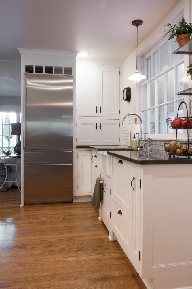 A kitchen with white cabinets , a stainless steel refrigerator , a sink , and a window.