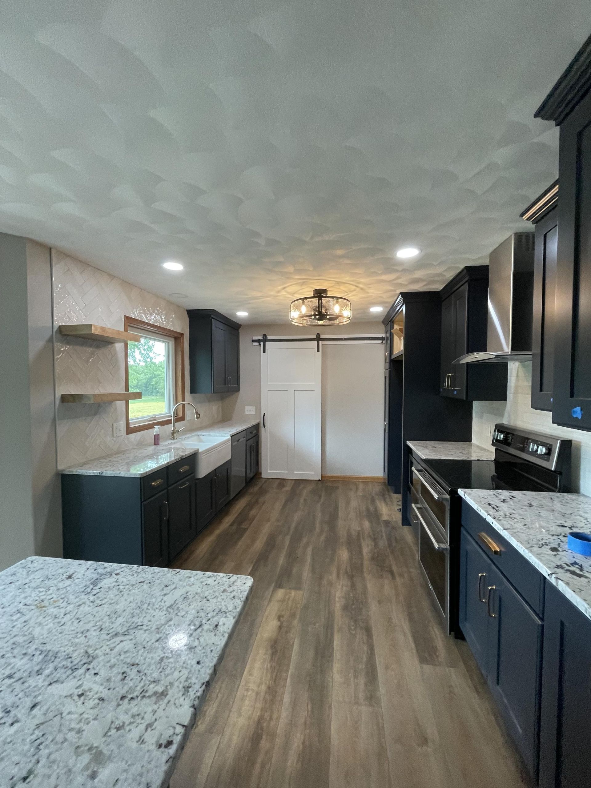 A kitchen with black cabinets , granite counter tops , stainless steel appliances and a large window.