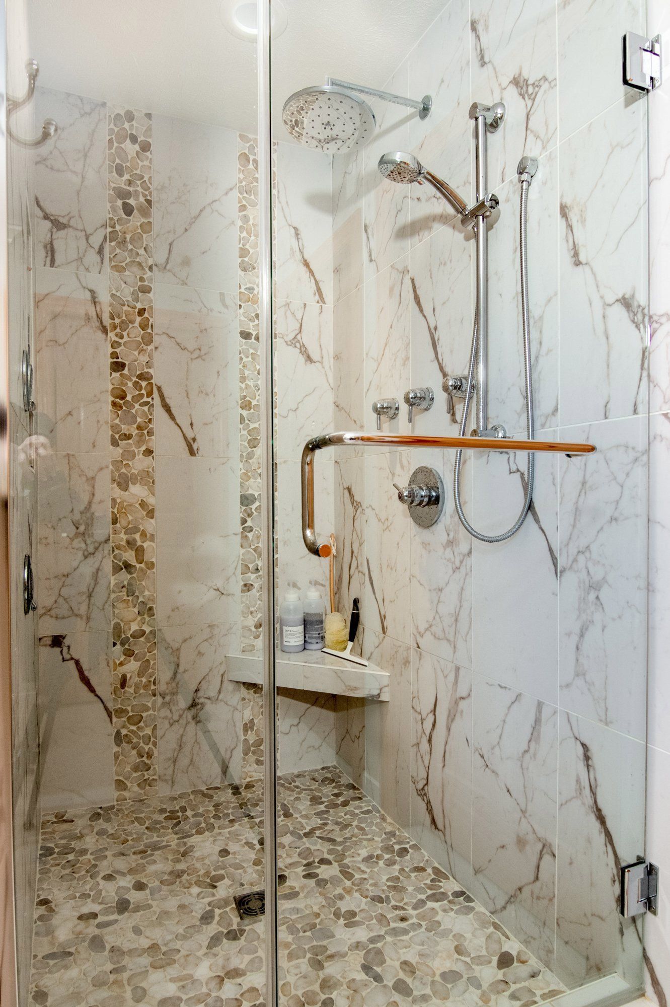 A walk in shower with a glass door and marble walls.
