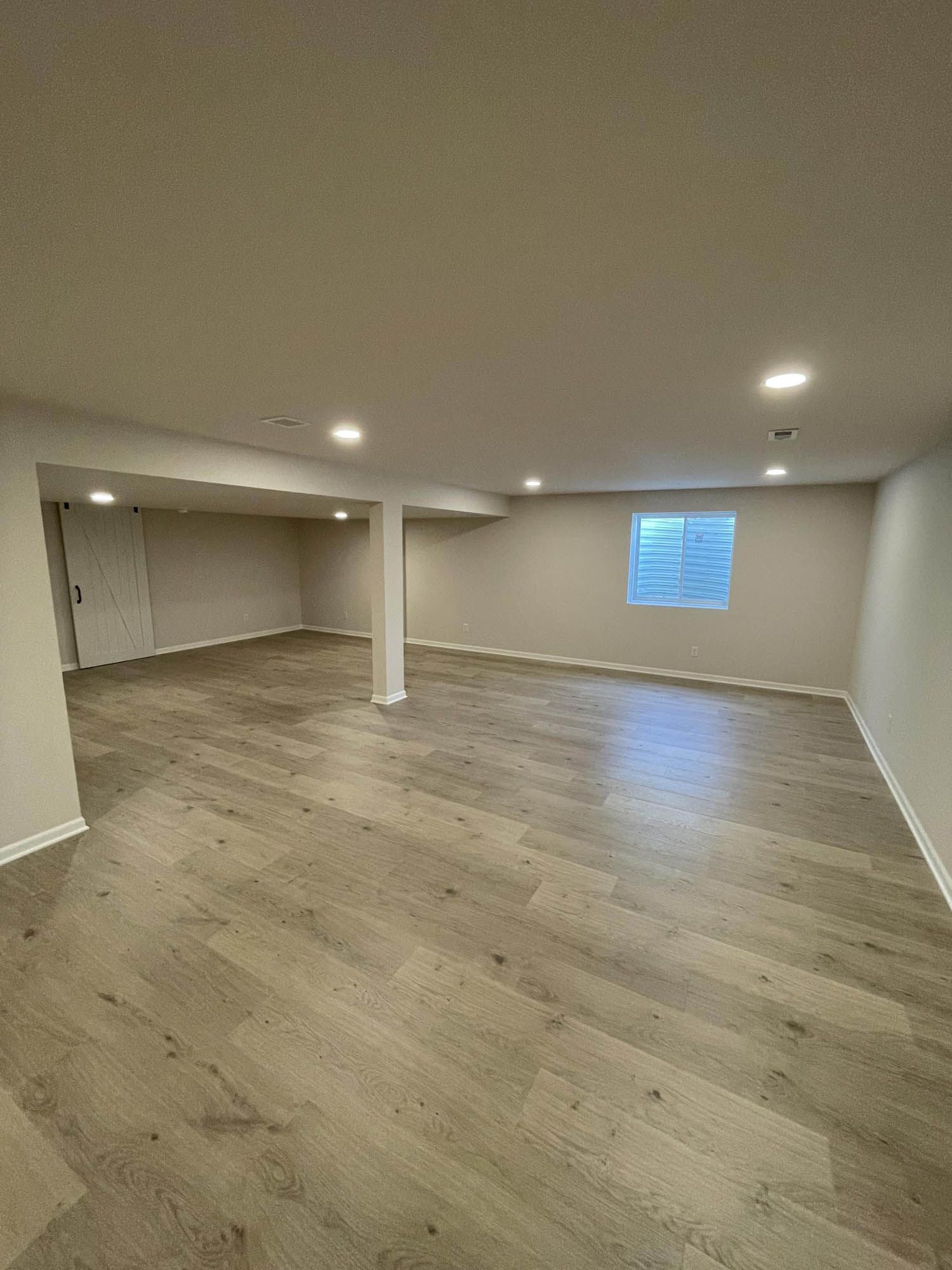 An empty basement with hardwood floors and a window.